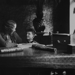 fotografia Jozefa Sedláka z cyklu „Latency”; przedstawia od lewejkobietę i chłopca siedzących przy stule, fotografia jesr czarno-biała